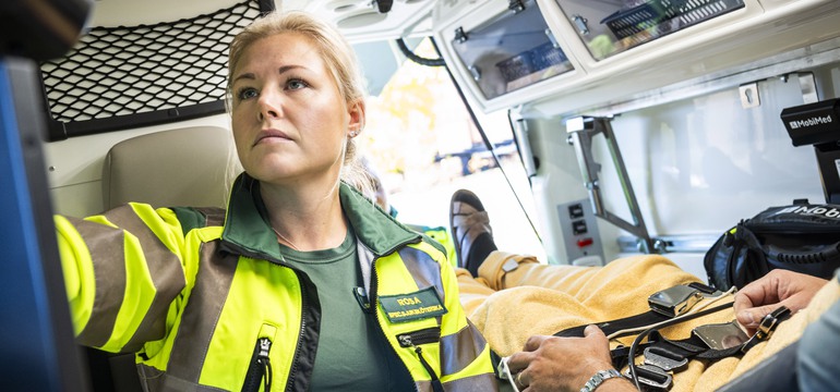 En specialistsjuksköterska sitter i ambulansen bredvid en patient.