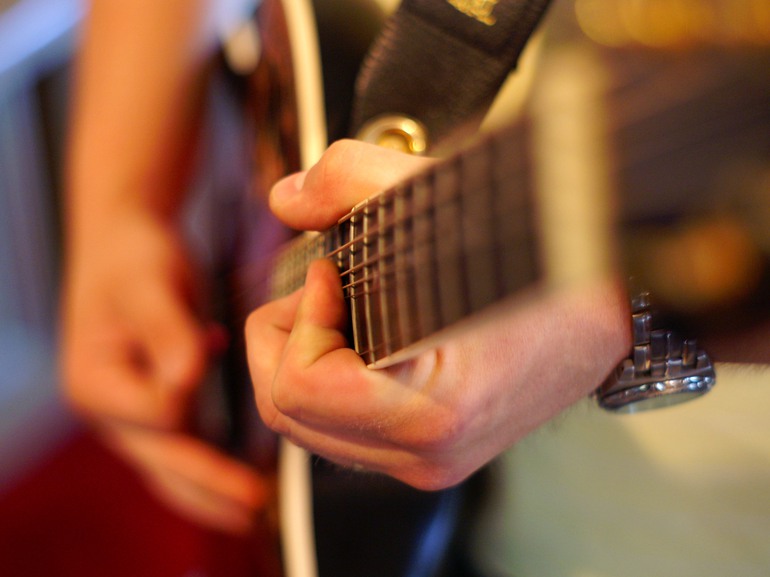 Närbild på händerna på en person som spelar gitarr