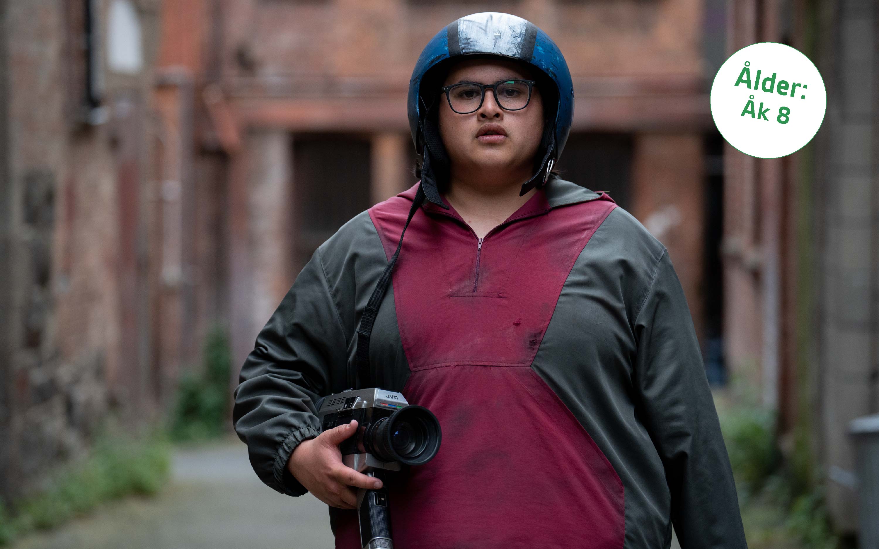En ung man med filmkamera under armen och en klotrund hjälm på huvudet, bild ur filmen Uproar