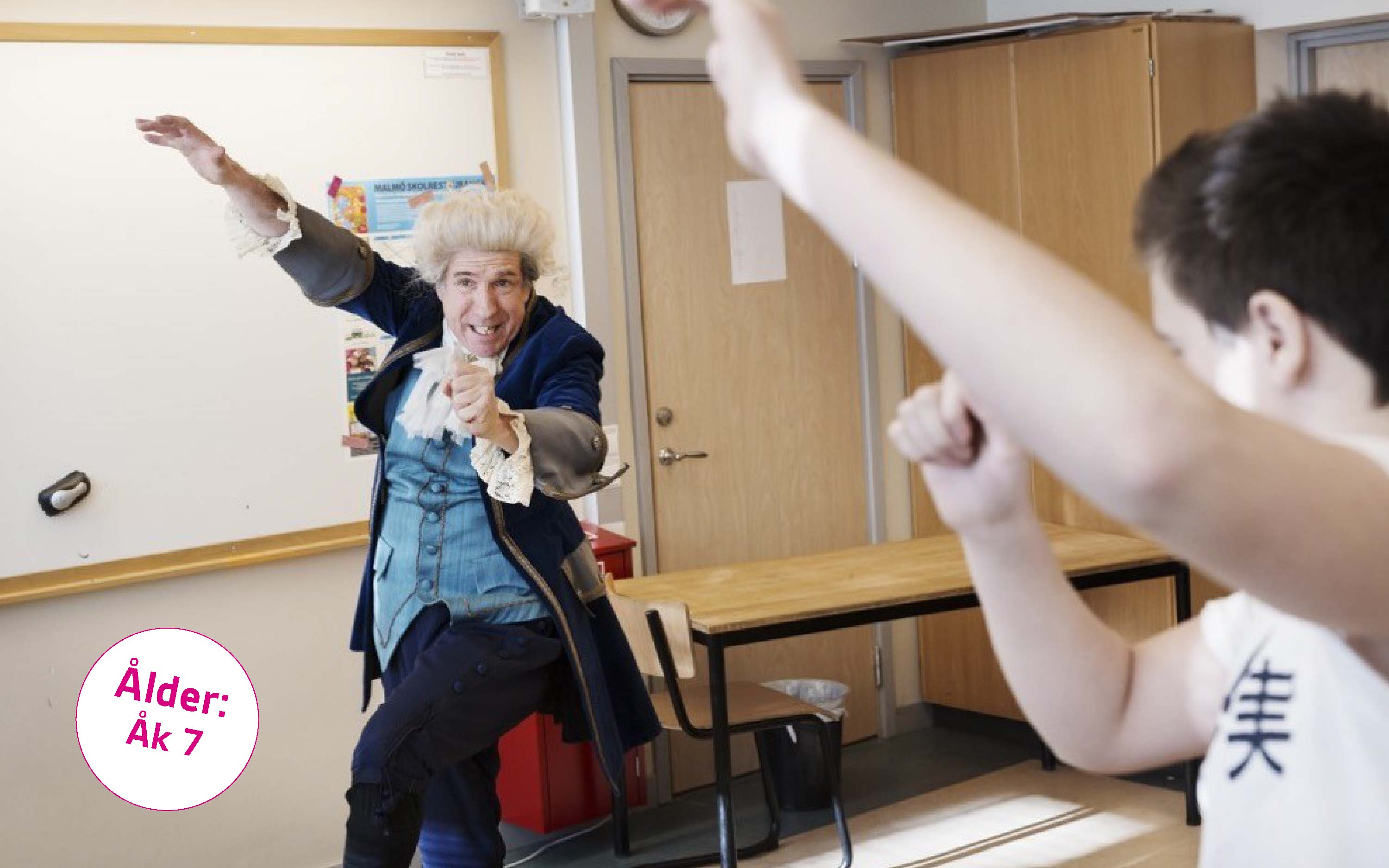person i 1770-talskläder dansar i ett klassrum omgiven av elever