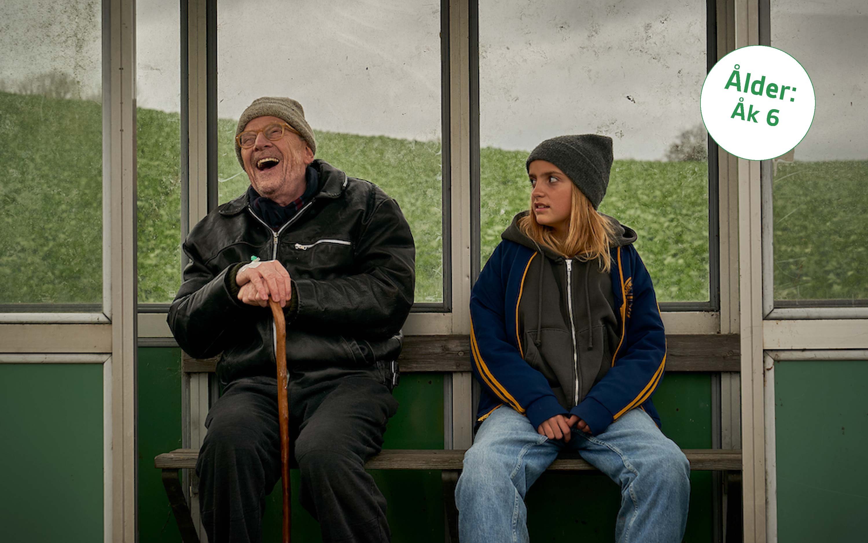 två personer i en busskur, en äldre man och en yngre flicka