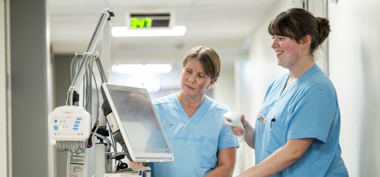En undersköterska och en sjuksköterska står vid en EKG-apparat.