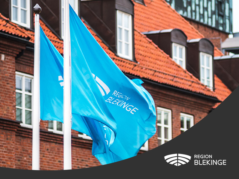 Närbild på Region Blekinges blåa flaggor. I nederkant en svart våg med Region Blekinges vita logotyp.