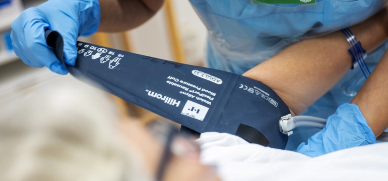 En undersköterska kontrollerar blodtrycket på en patient i en sjukhussäng.