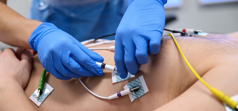 En person i blå handskar fäster elektroder på en patient.