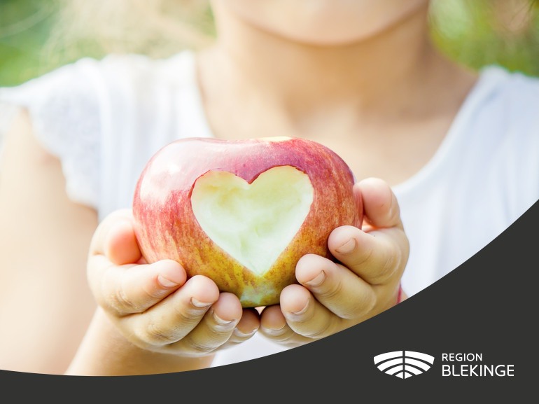 En person håller i ett äpple. Äpplet har ett hjärta utskuret i sig. 