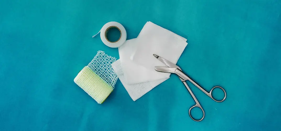 Bandage, kompresser och listersax ligger på en blå duk.