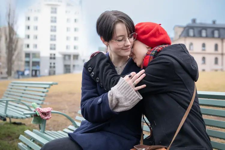 Två personer som sitter på en parkbänk och kramas.